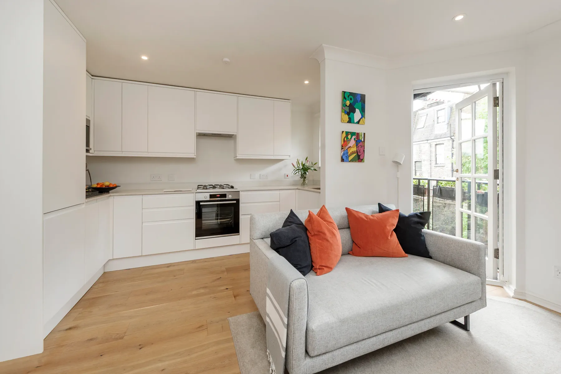 A bright open-plan living area with a compact kitchen and gray seating.