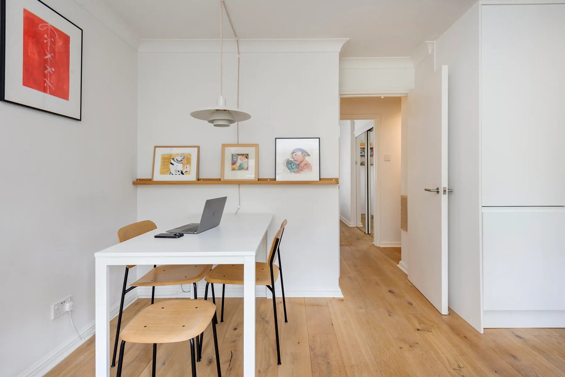 A bright dining area with a white table and framed artwork on a shelf.