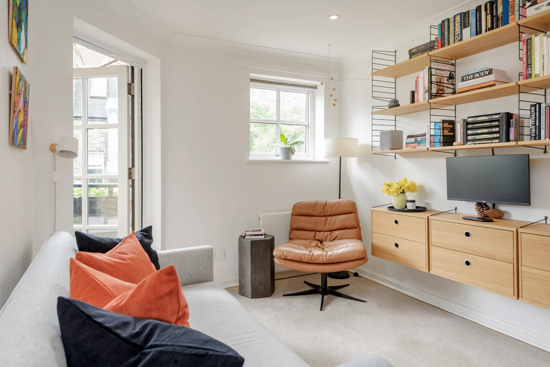 A bright living room with a sofa, lounge chair, and wall-mounted shelves.