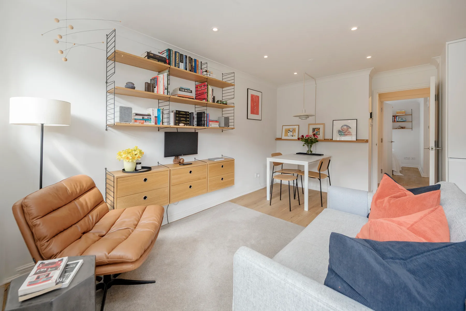 A bright living room with a television, shelving, and a small dining table.