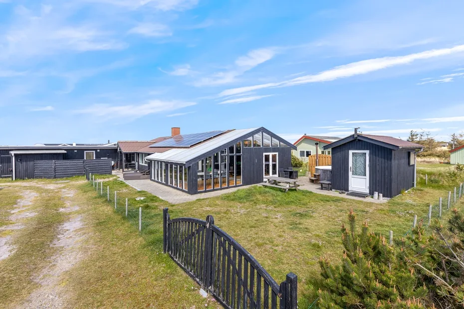 A modern glass-fronted building stands beside a dark shed in an open grassy yard.