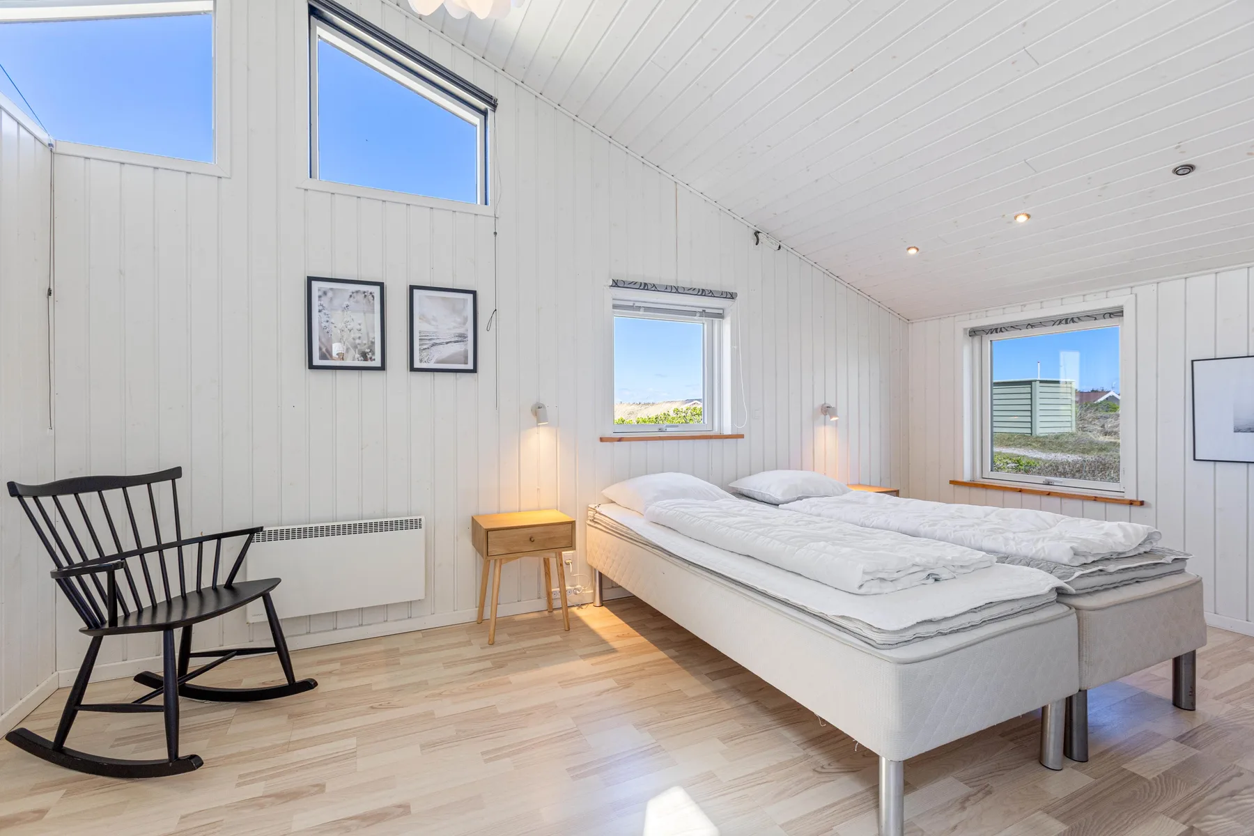 A bright bedroom with a double bed, a rocking chair, and windows.
