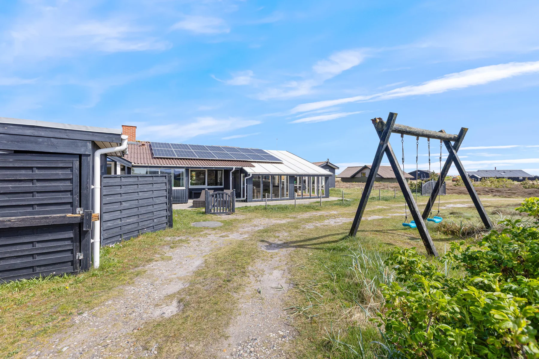 A low house with solar panels sits beside a grassy yard and wooden swing set.