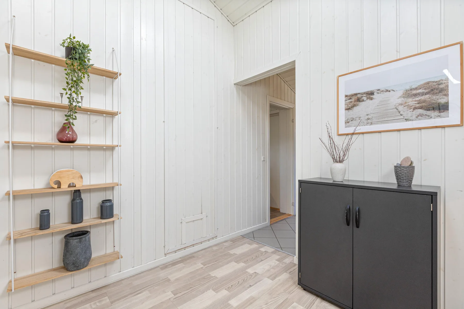 A bright entryway with a dark cabinet, wall shelves, and a framed landscape print.