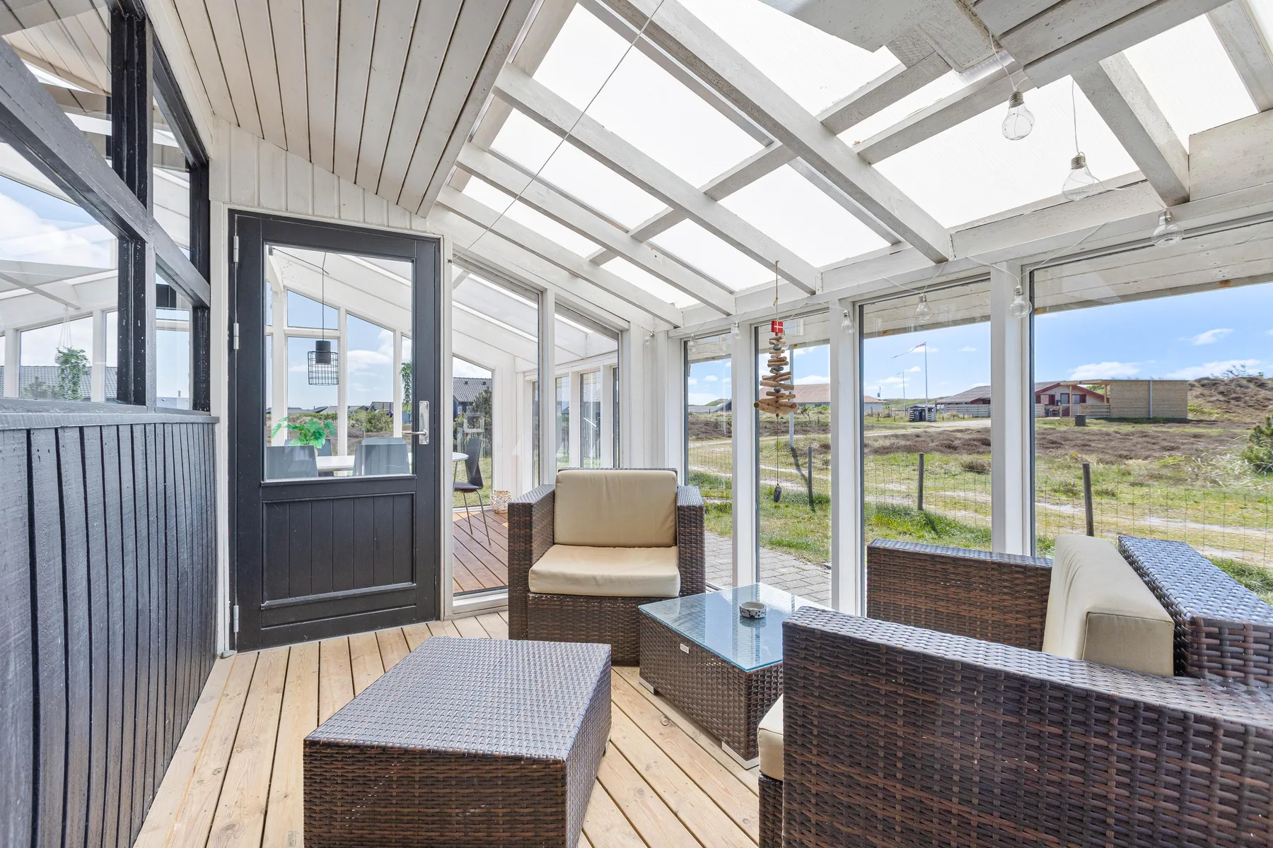 A bright glass-enclosed sunroom with wicker seating and views of the yard.