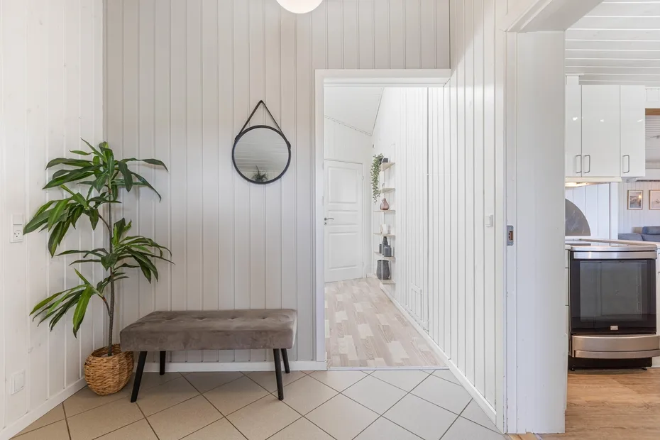 A bright entryway with a bench, a potted plant, and a round wall mirror.