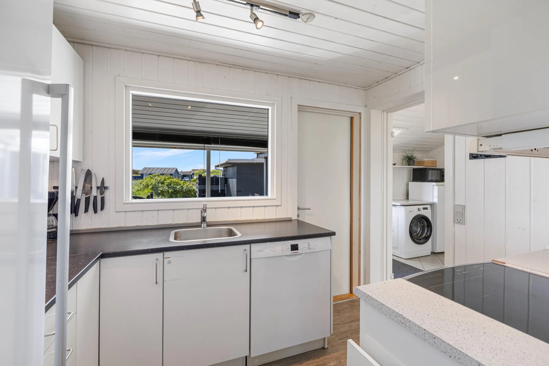 A bright kitchen with white cabinets, a sink, and a window overlooking greenery.