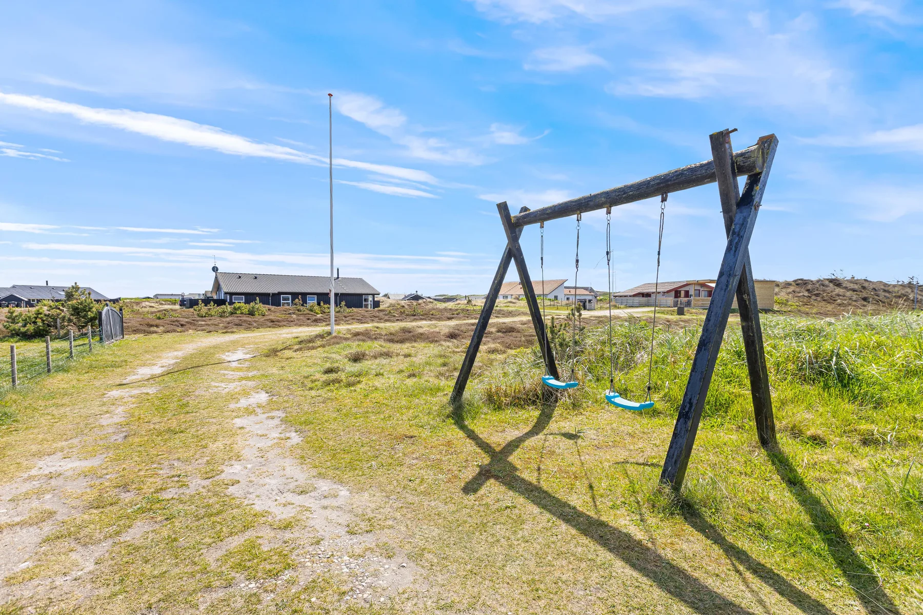 A grassy outdoor area with a wooden swing set beside a sandy path.