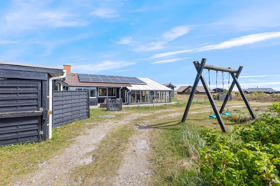 A modern house with solar panels stands beside a gravel path and outdoor swing.