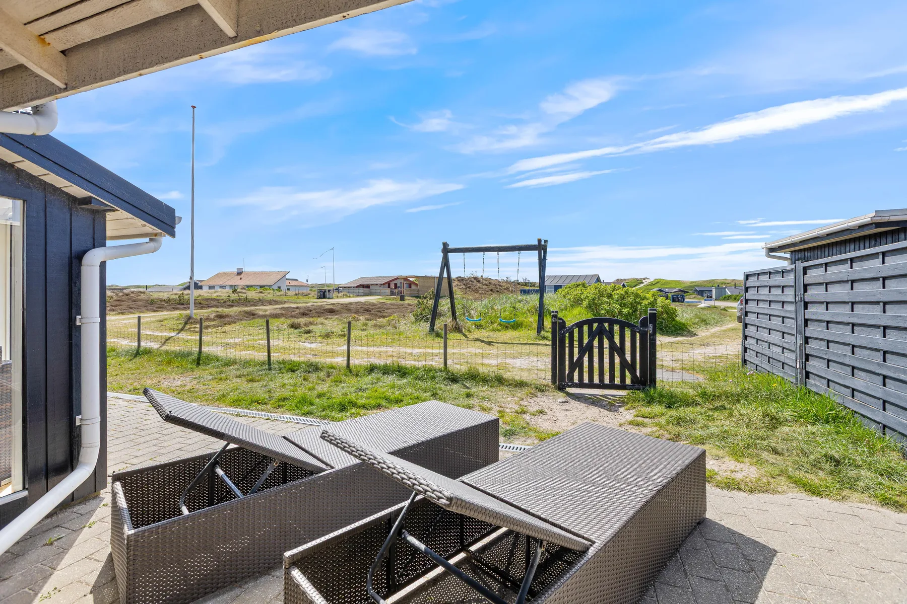 A patio with outdoor seating overlooks a grassy yard and fenced path.