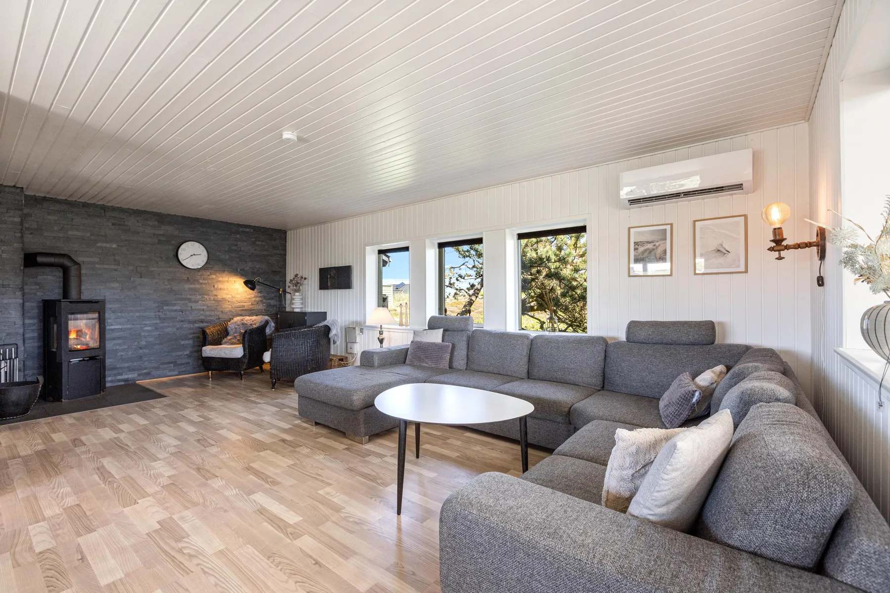 A bright living room with gray seating and a fireplace along the dark wall.