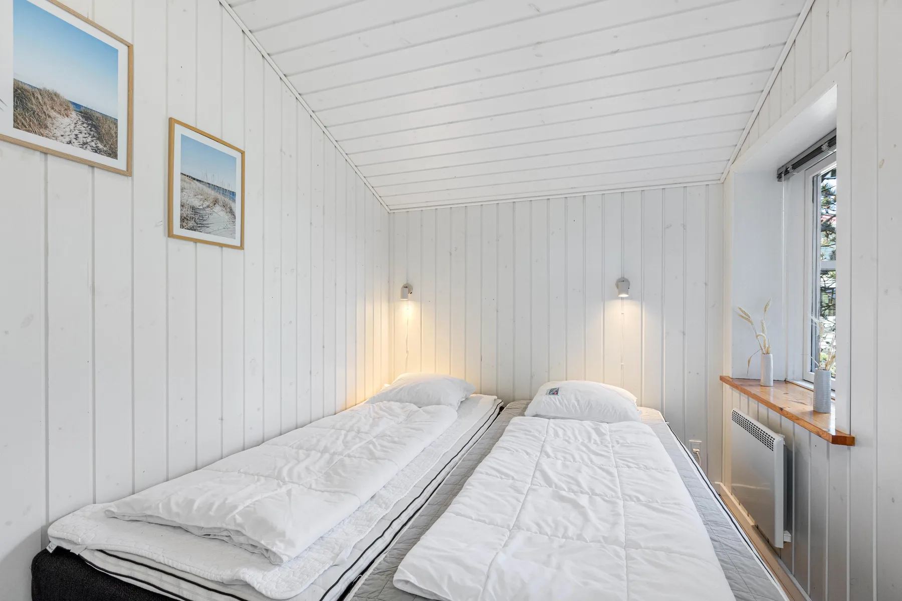 A bright bedroom with two single beds and framed pictures on the wall.