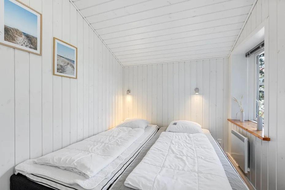 A bright bedroom with two single beds and wall-mounted lights.