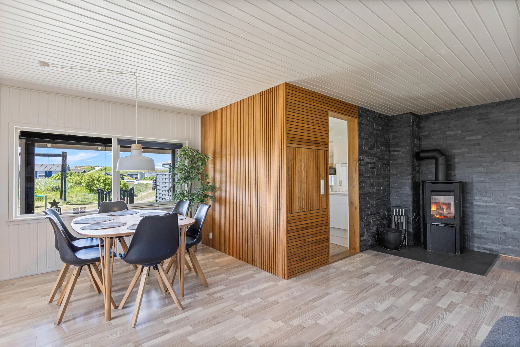 A dining area beside a wood-paneled partition and a dark stone fireplace wall.