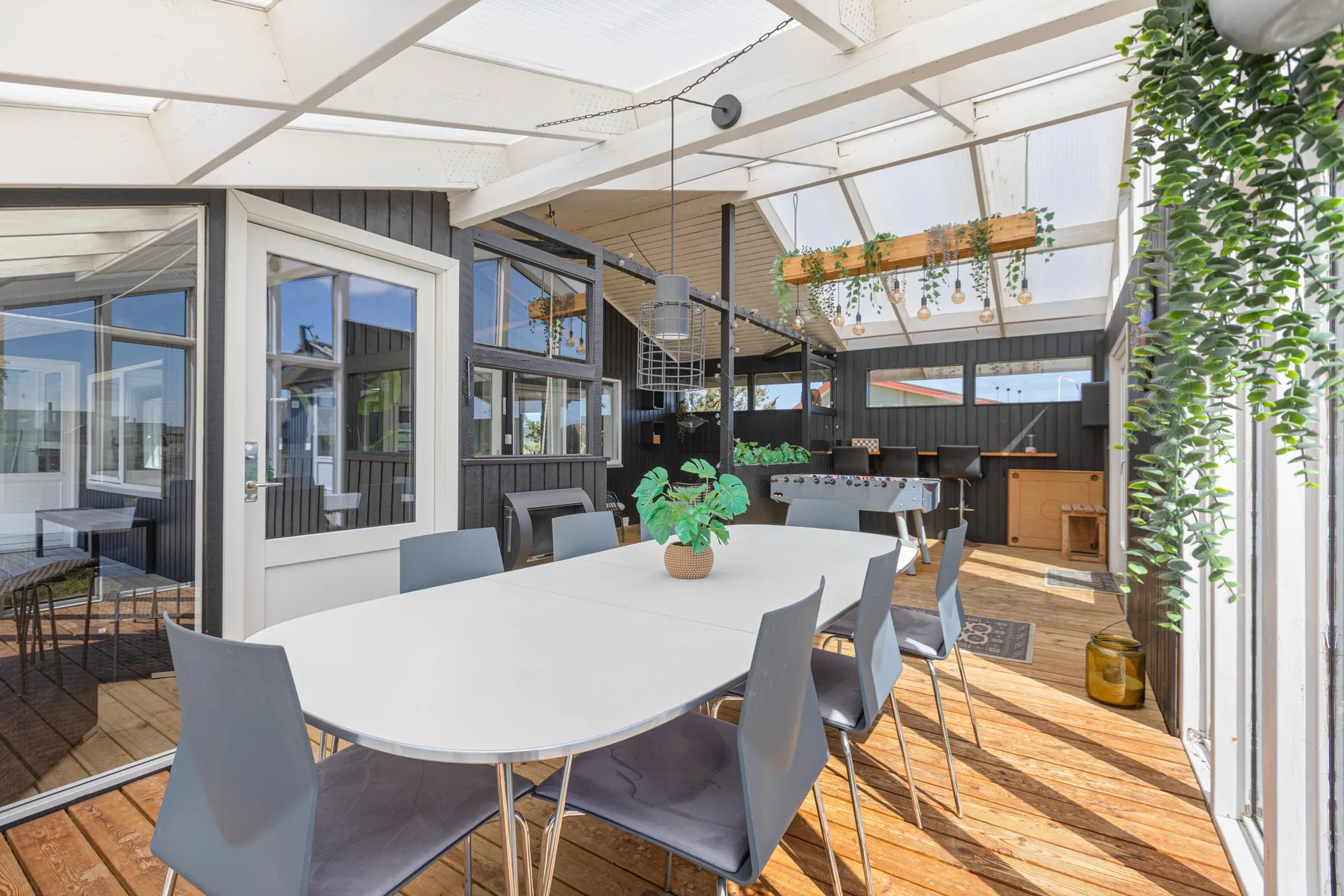 A bright dining area with a long table and gray seating beside large windows.