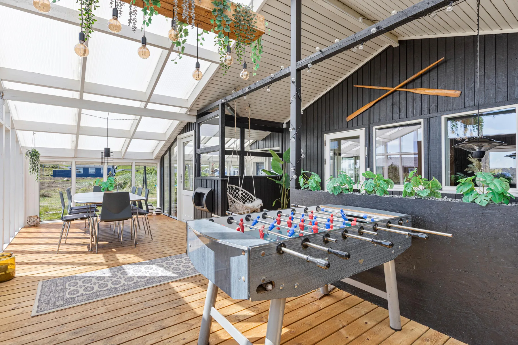 A bright enclosed patio has a foosball table beside a dining area.