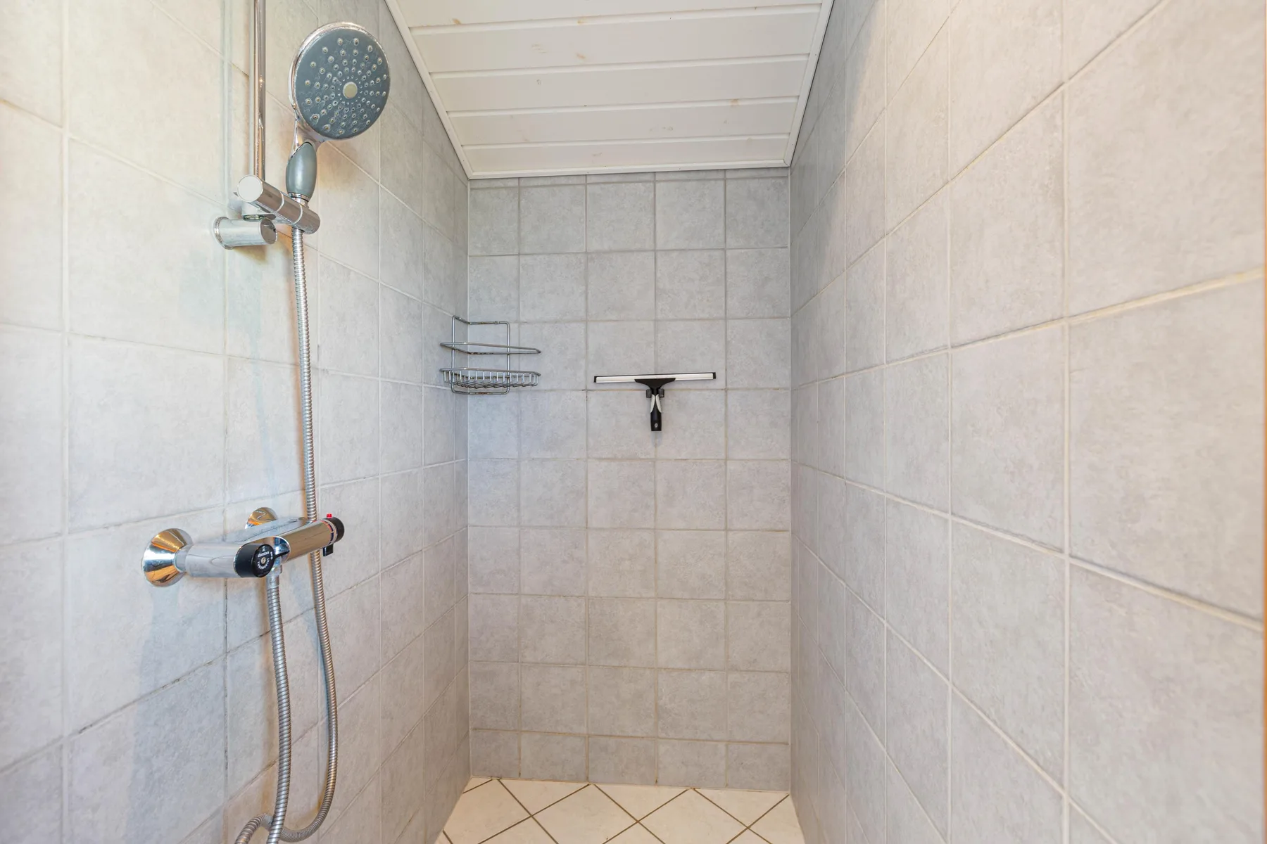 A tiled shower with a wall-mounted showerhead and controls.