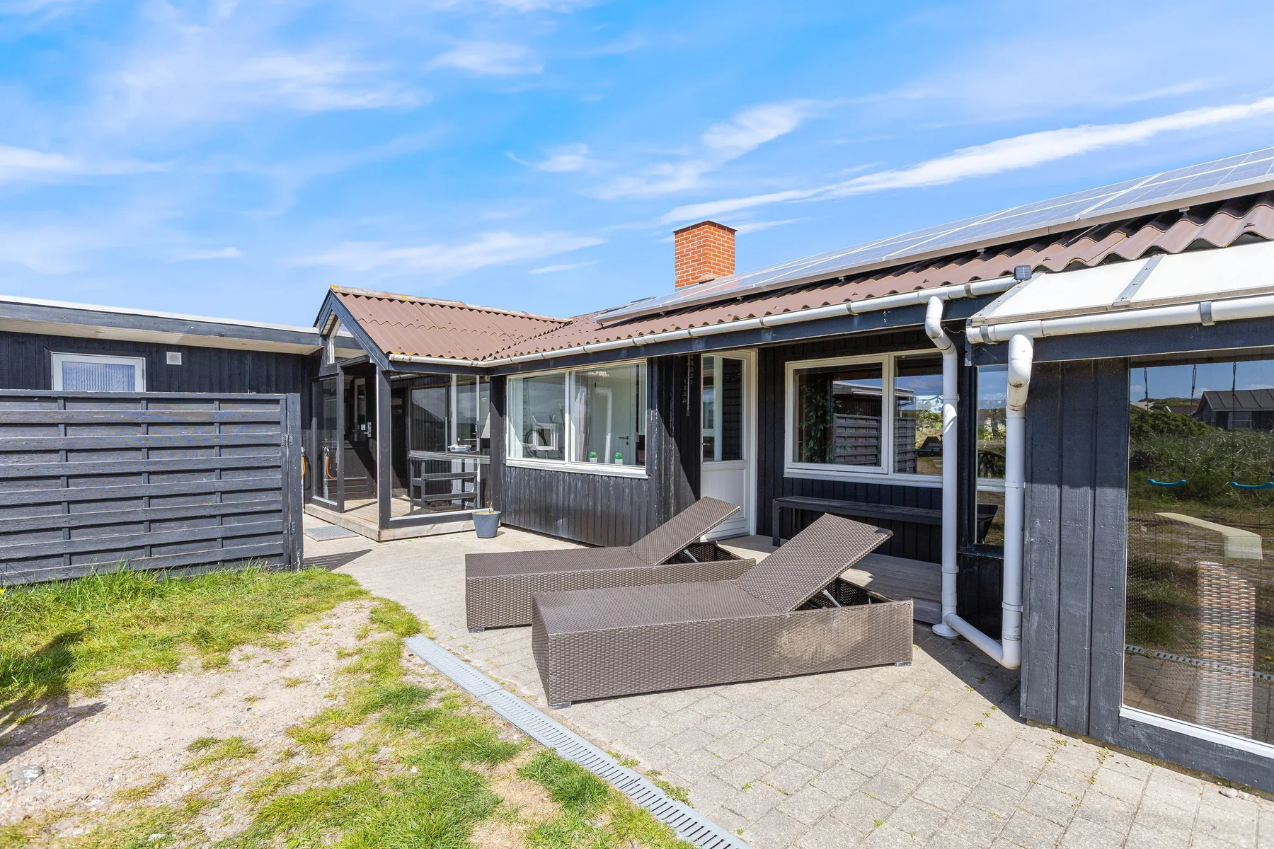 A low house opens onto a paved patio with outdoor seating.