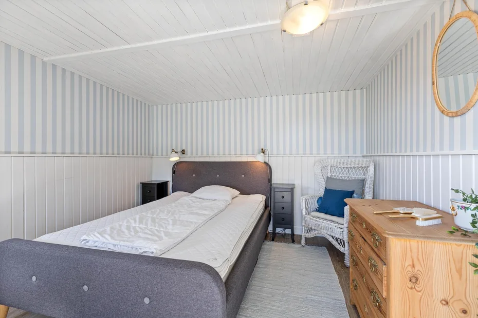 A bedroom with a double bed, a wicker chair, and a wooden dresser.