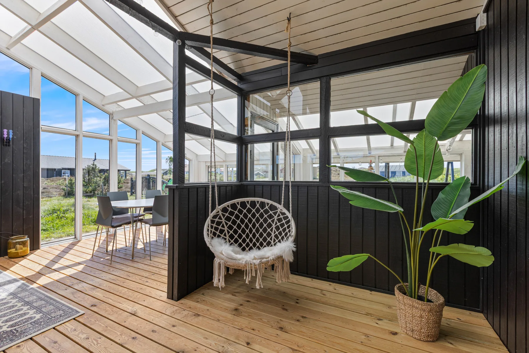 A bright sunroom with a hanging chair and large windows.