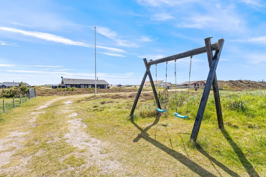 An outdoor swing set stands beside a grassy path with low buildings in the distance.