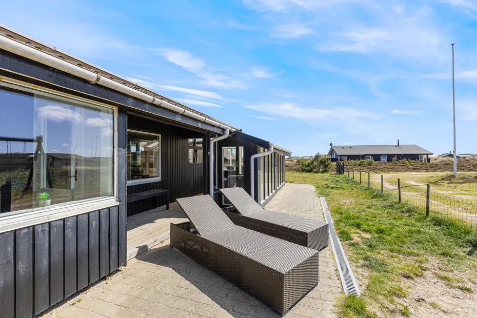 A dark-sided building opens onto a paved patio with outdoor seating beside a grassy field.
