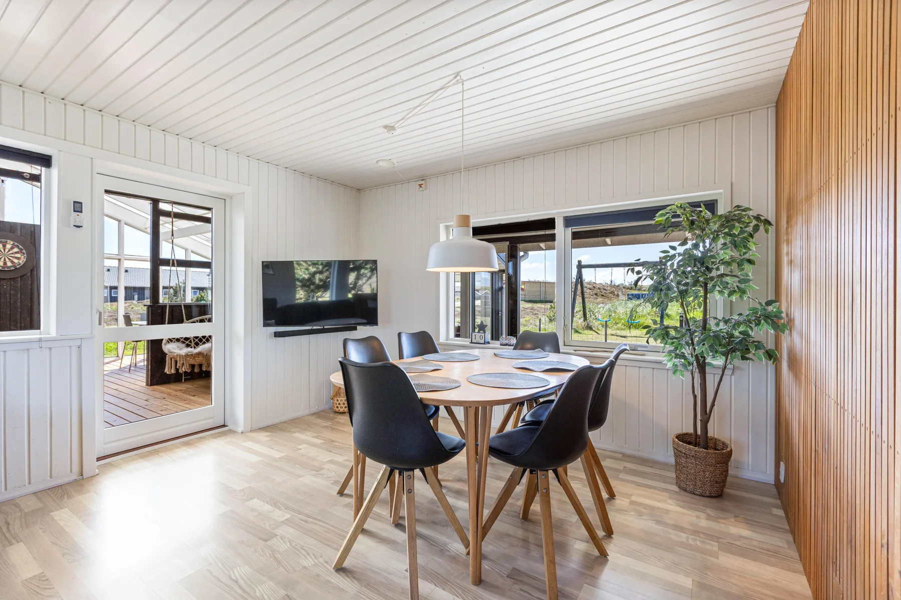 A bright dining area with a wooden table, dark seating, and large windows.