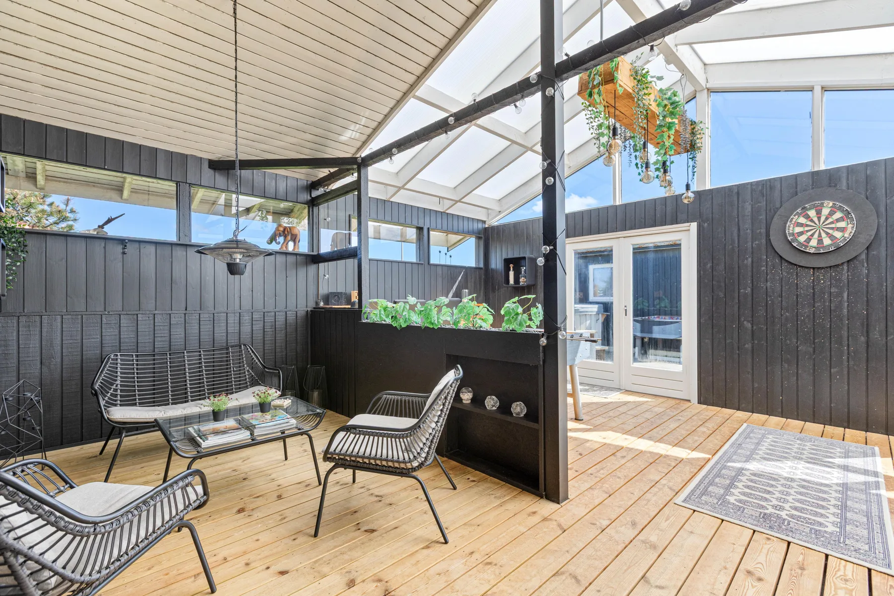 A bright enclosed patio with seating, potted plants, and a dartboard.