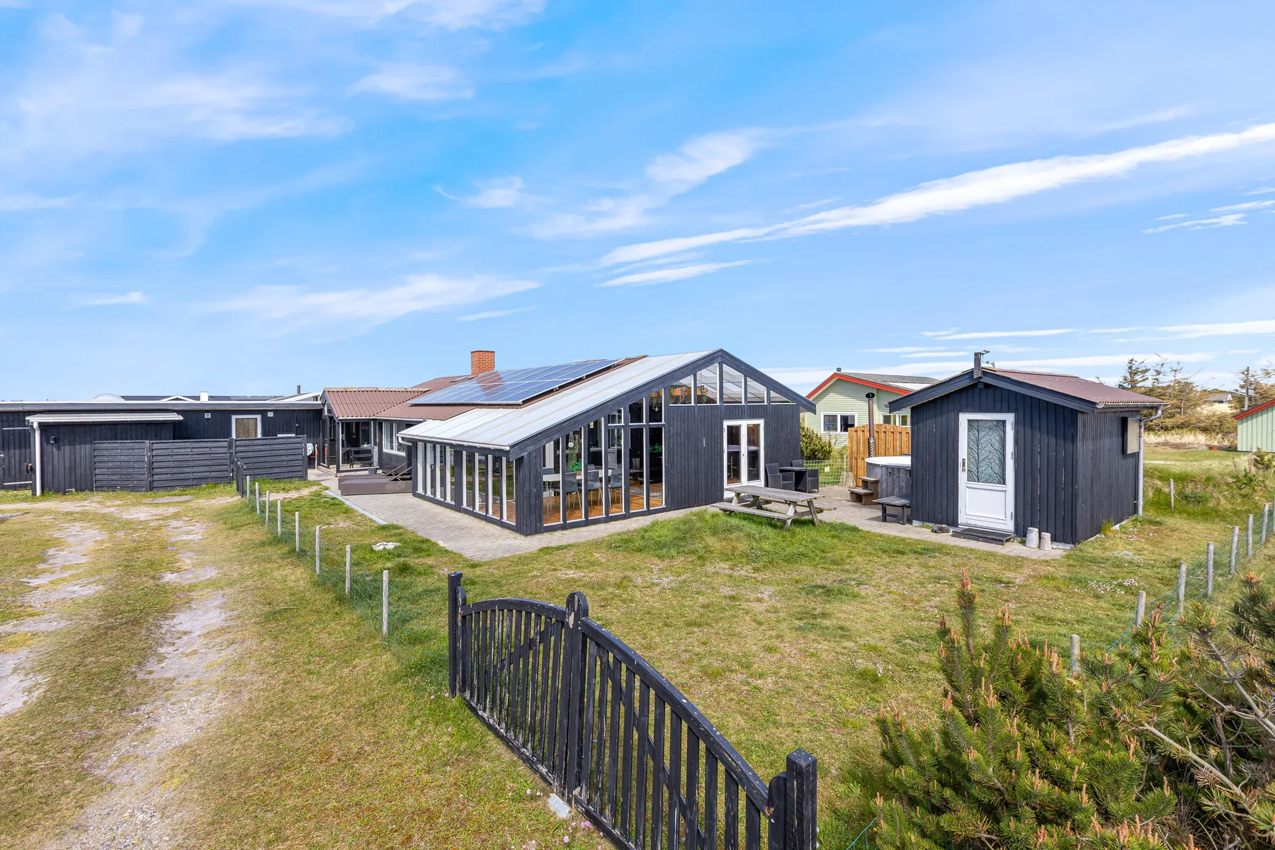 A modern house and detached outbuilding stand in a grassy yard under a blue sky.