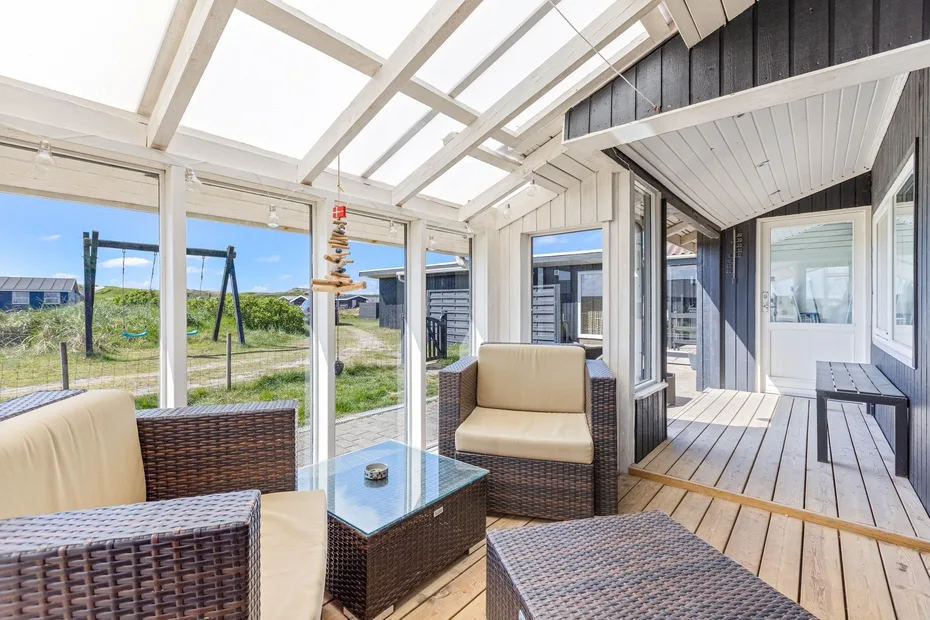 A covered patio with cushioned seating and large windows overlooking a grassy yard.