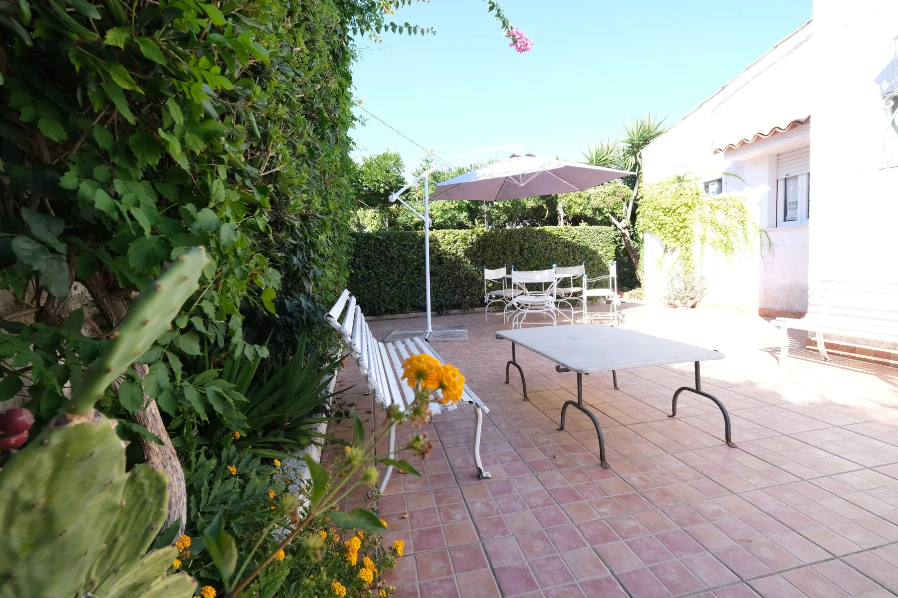 Patio exterior embaldosado con una mesa, asientos y una sombrilla.