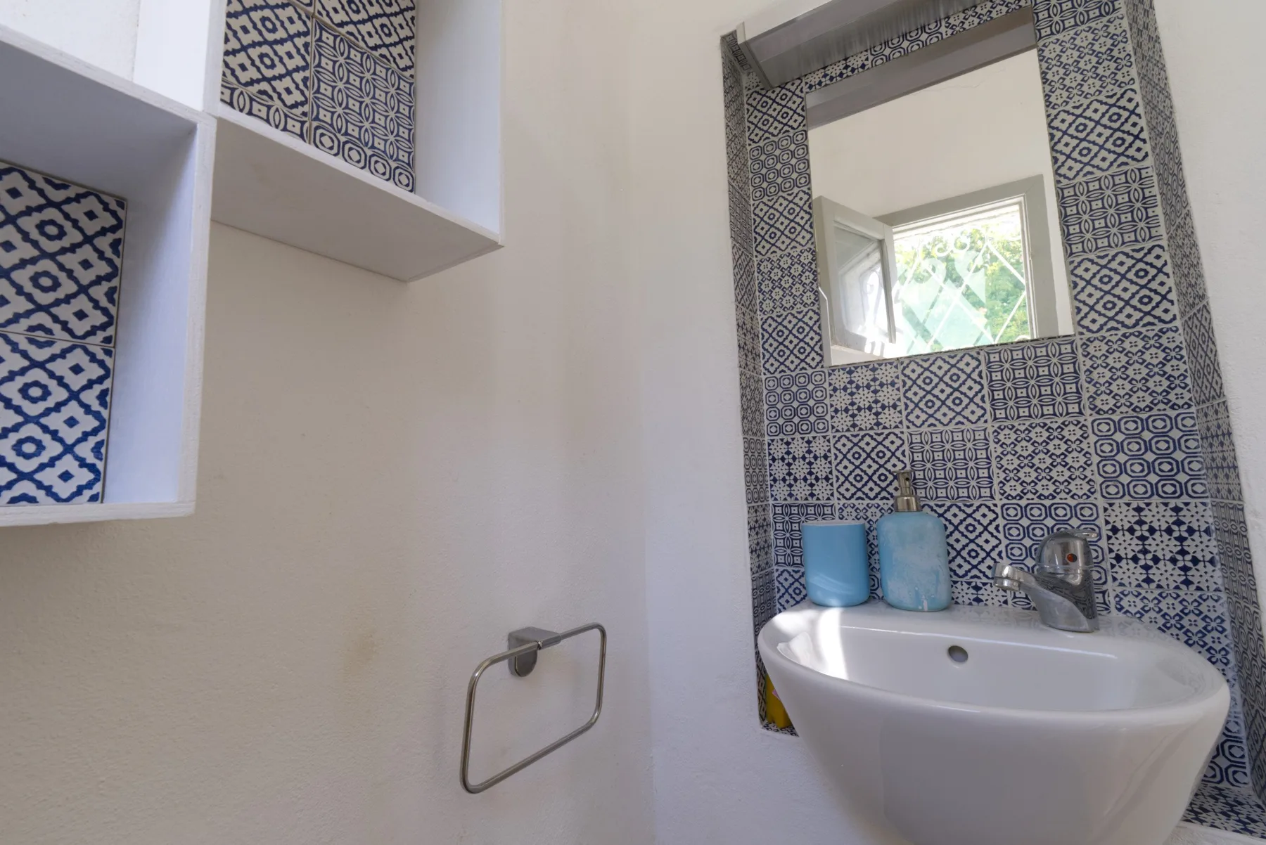 A bathroom sink and mirror are set against a wall of patterned tiles.