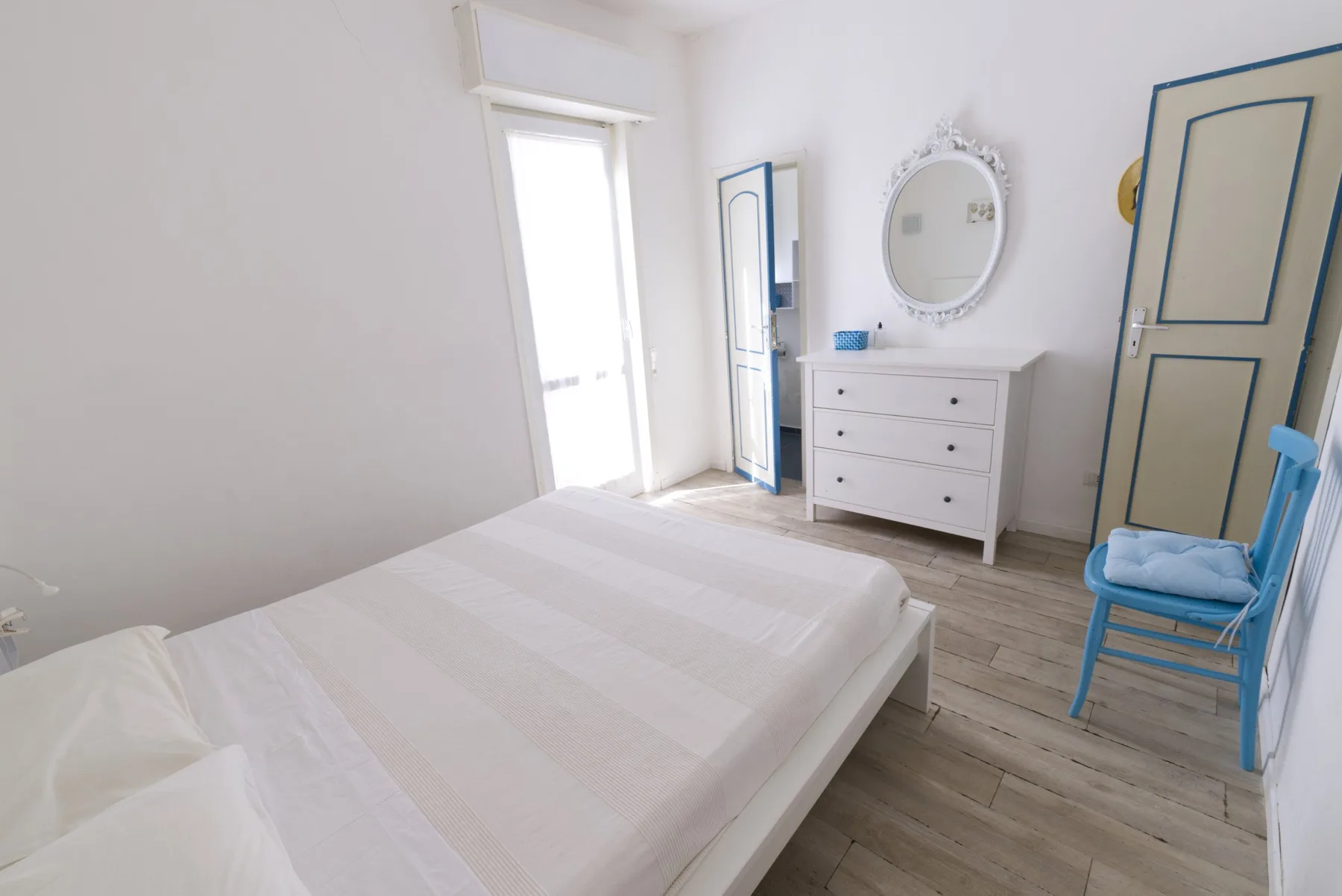 A bright bedroom with a bed, a dresser, and a blue chair.