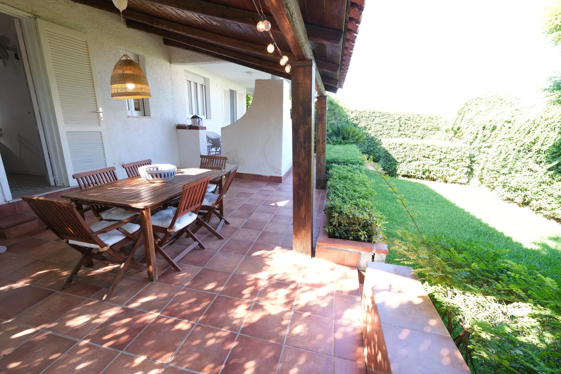 A covered outdoor dining area opens onto a green garden.