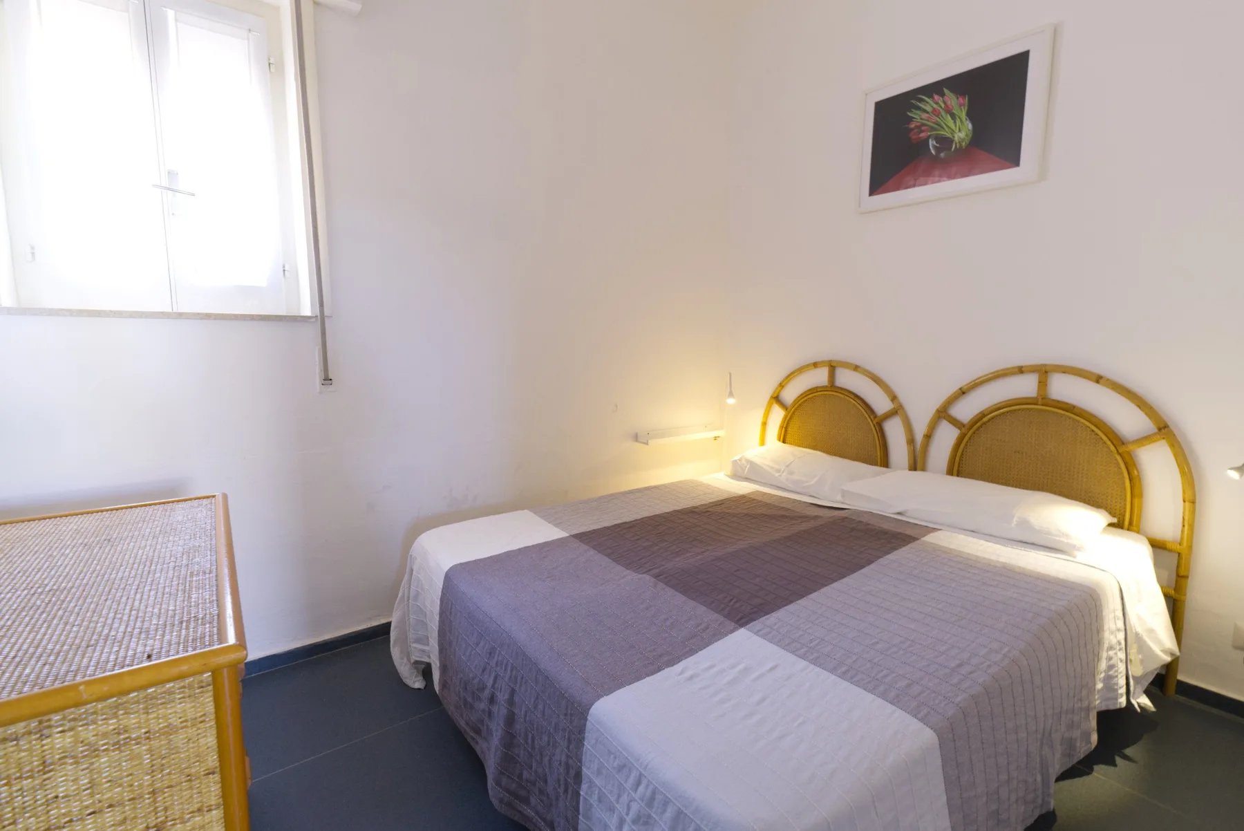 A bedroom with a bed beneath a framed floral picture.