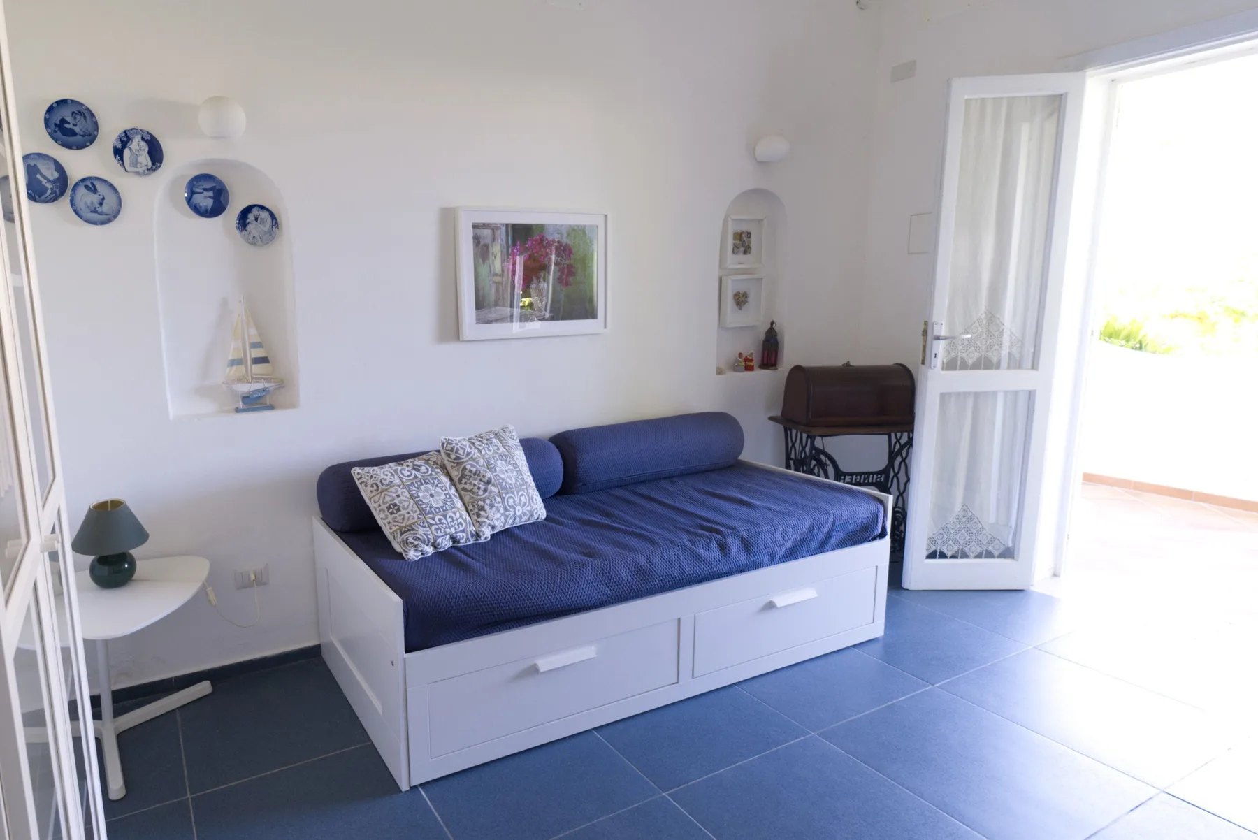 A bright bedroom with a blue daybed and an open glass door.