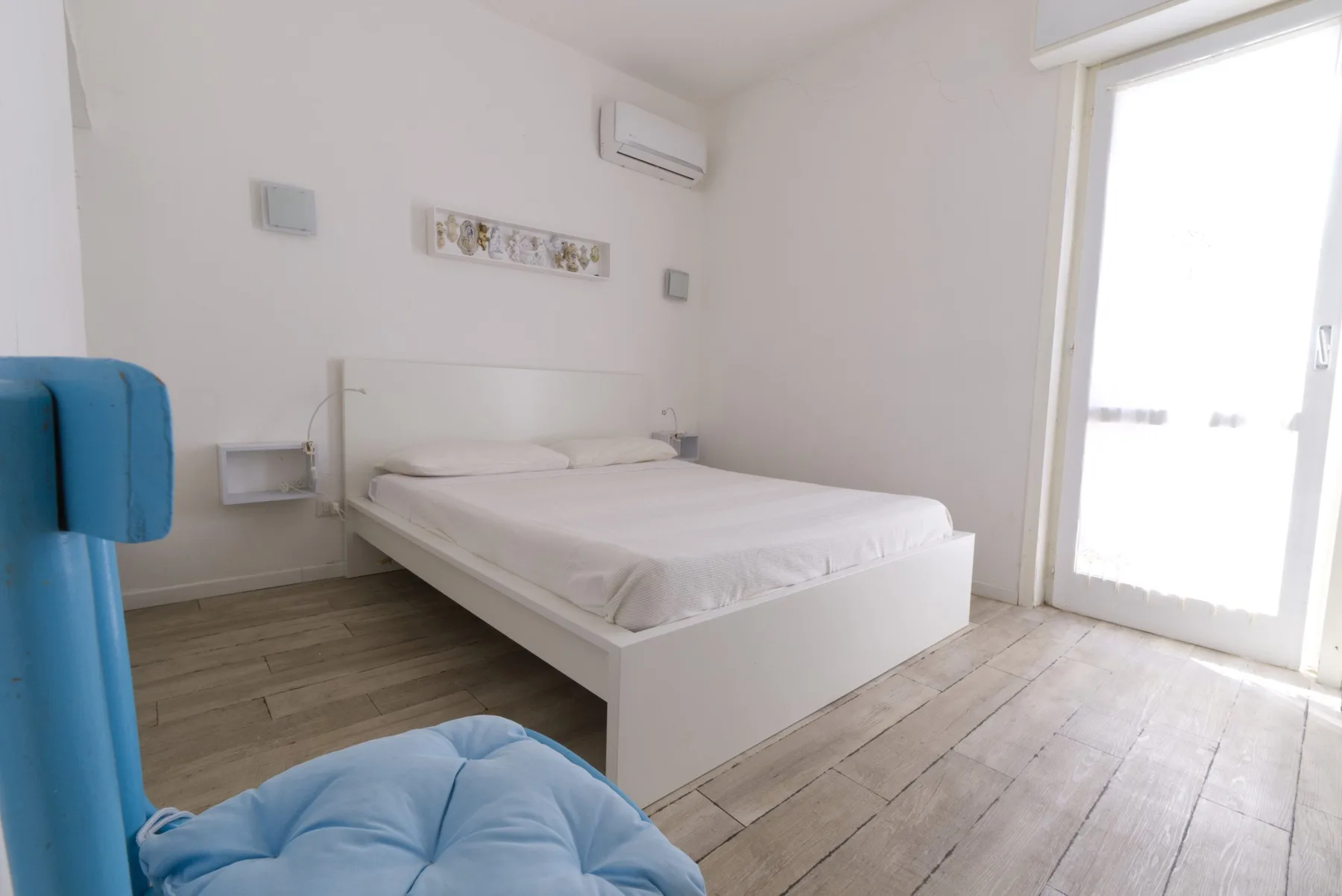 A bright bedroom with a bed, pale walls, and a glass door.