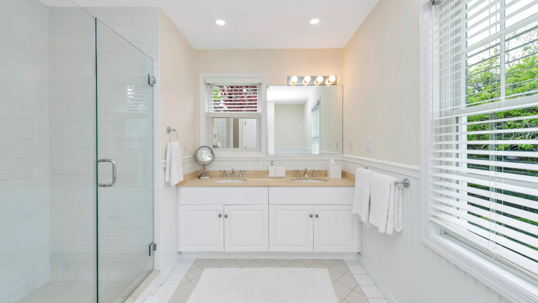 Un baño luminoso con ducha de vidrio y lavabo doble.