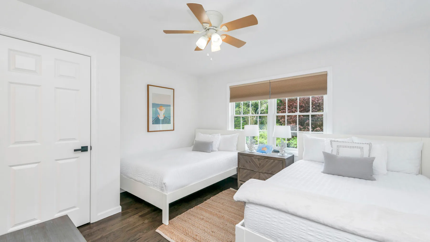 Un dormitorio luminoso con dos camas, una ventana y un ventilador de techo.