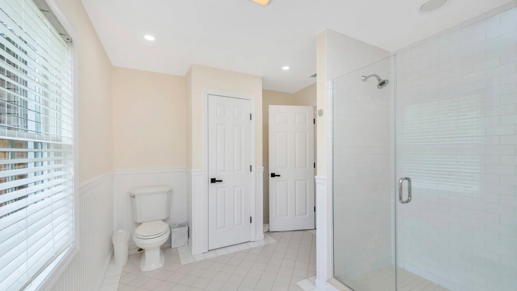 Un baño luminoso con ducha de cristal, inodoro y suelo de baldosas blancas.