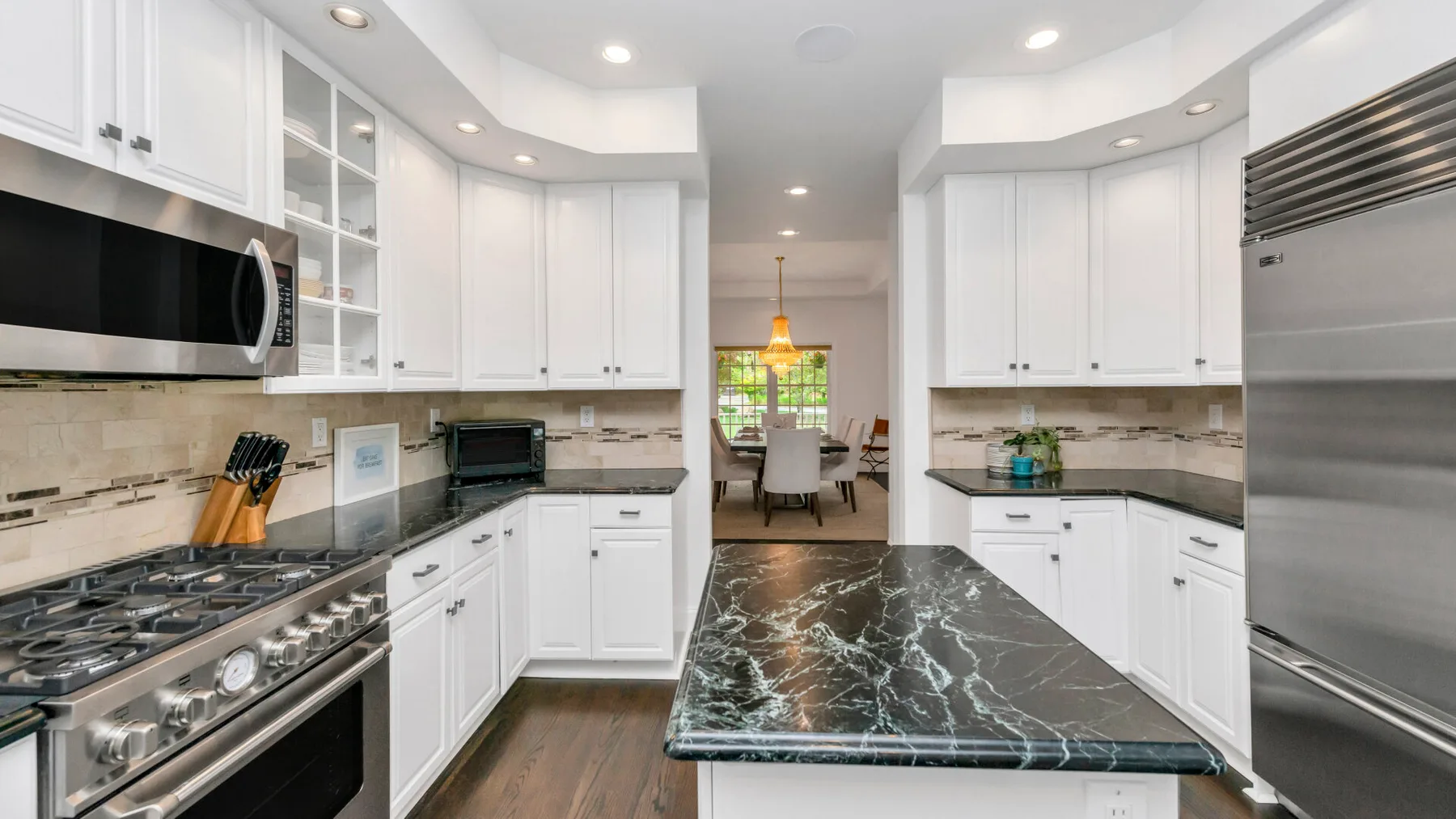 Una cocina luminosa con gabinetes blancos, encimeras oscuras y una larga isla central.