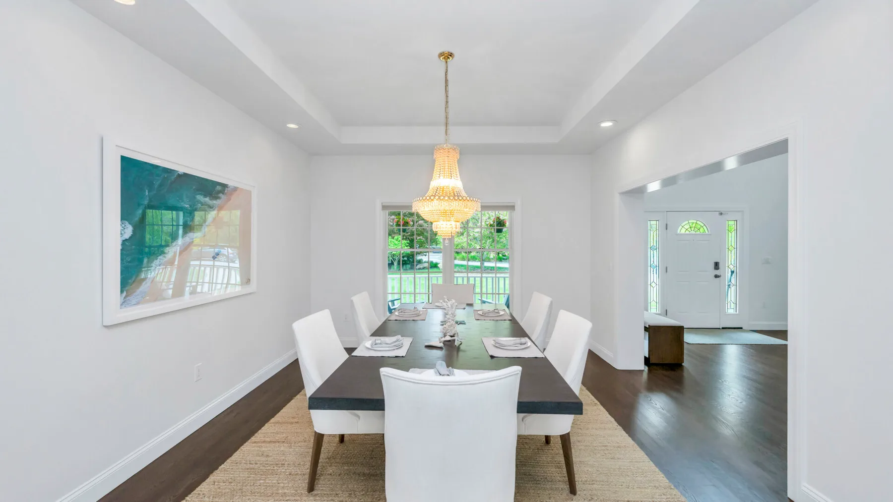 Un comedor luminoso con una mesa larga, asientos blancos y una lámpara de araña.