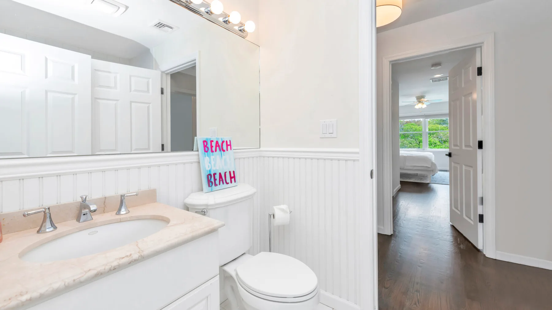 Un baño luminoso con lavabo y una puerta abierta hacia un dormitorio.