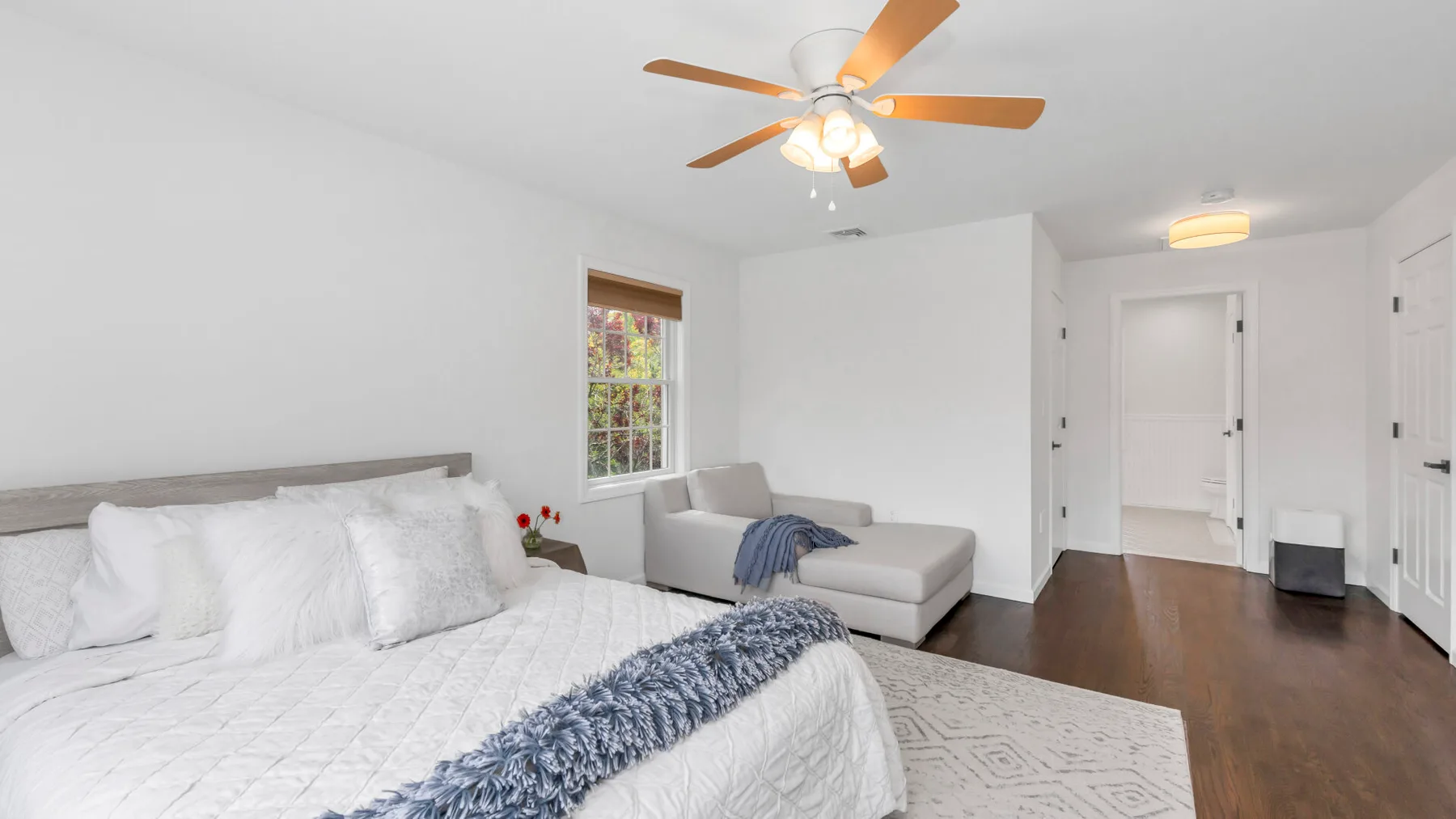 Un dormitorio luminoso con una cama, una pequeña zona de estar y un ventilador de techo.