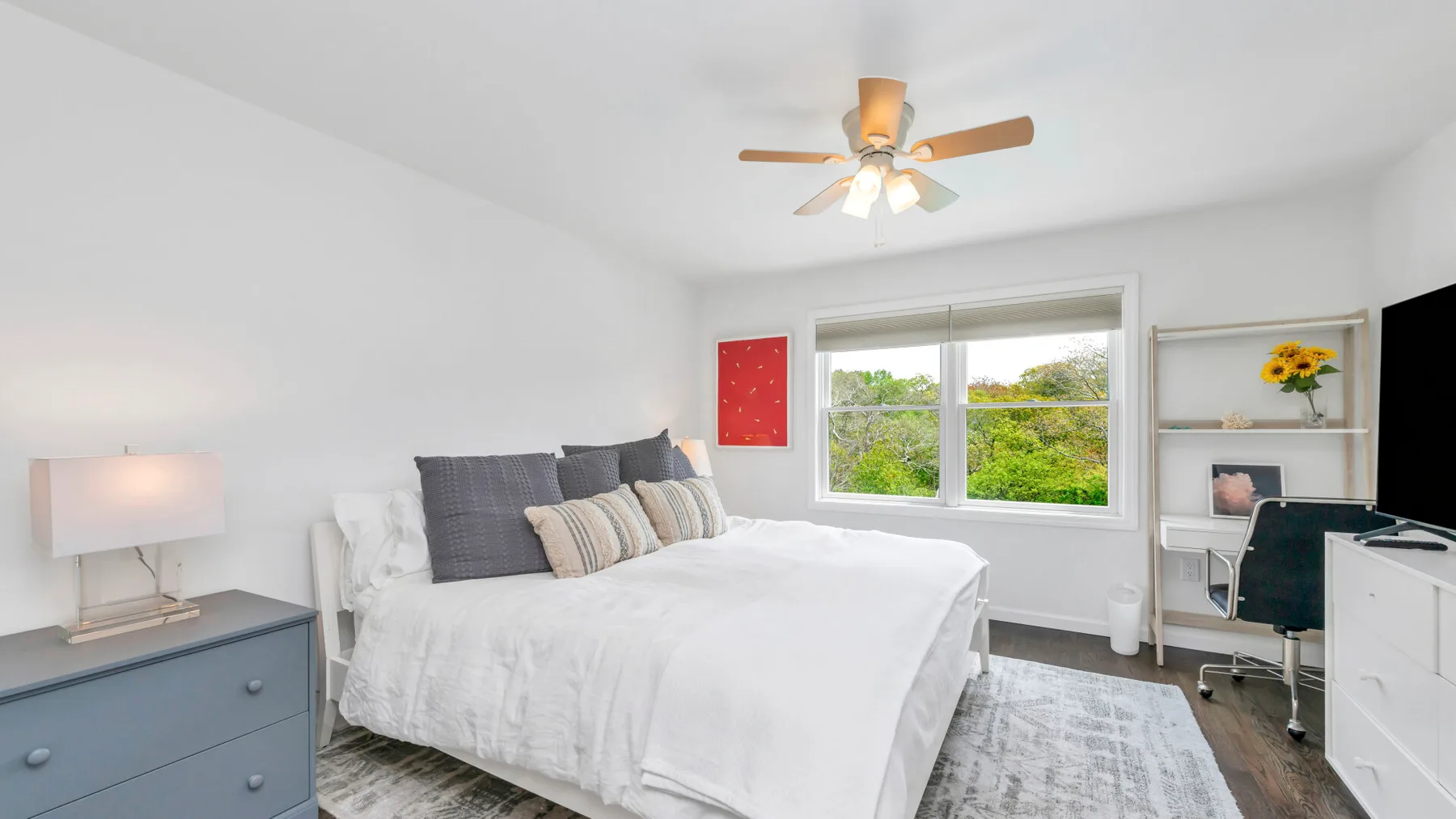 Un dormitorio luminoso con una cama blanca, una ventana amplia y una zona de escritorio.