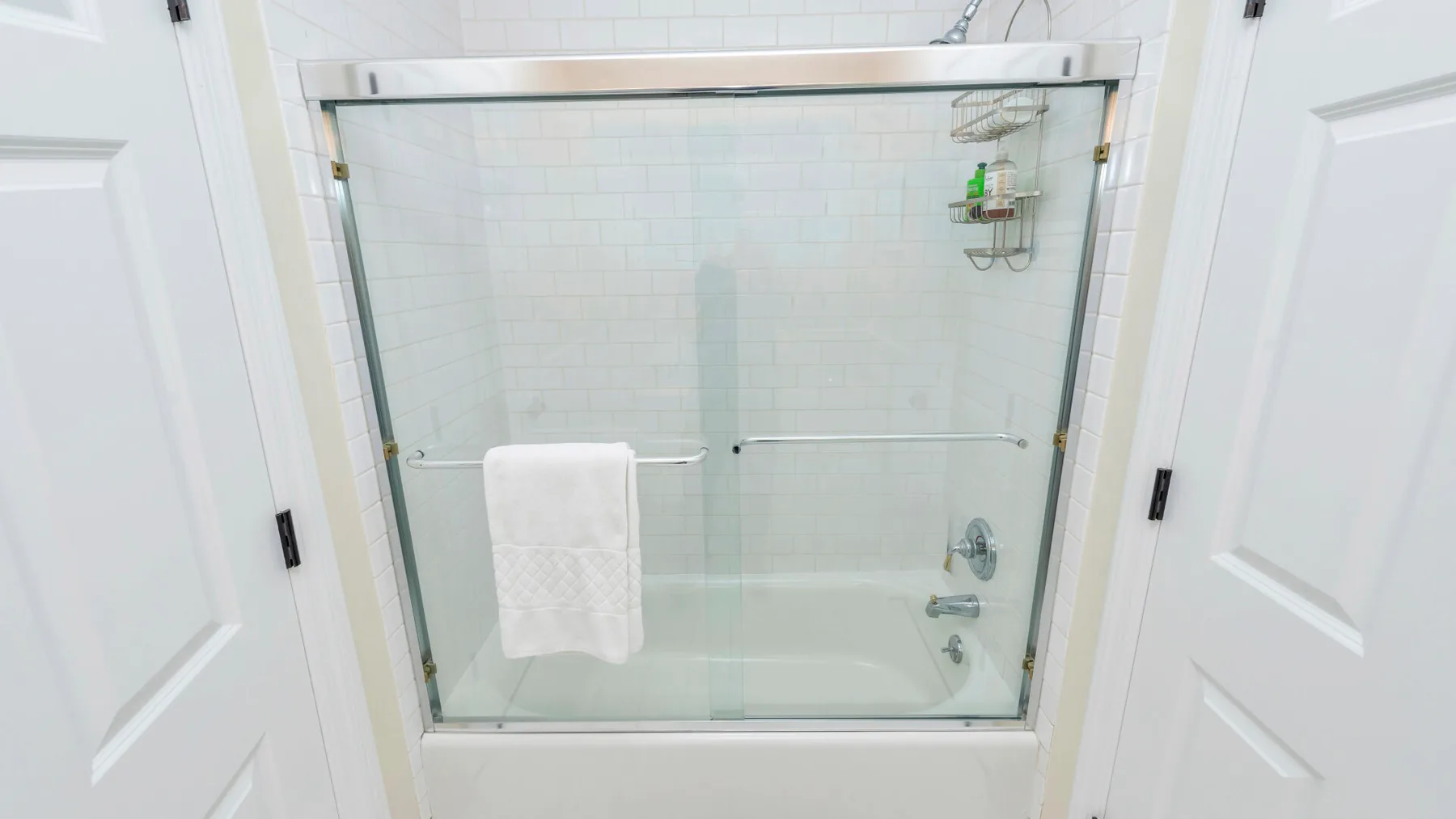Una ducha de baño con azulejos, mampara de vidrio y una toalla colgada dentro.