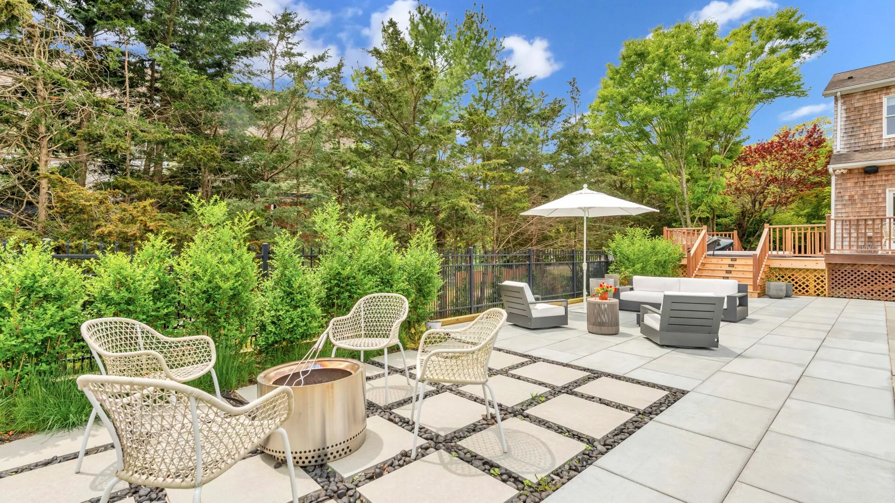 Un patio exterior pavimentado tiene asientos, una mesa y una sombrilla junto a una casa.