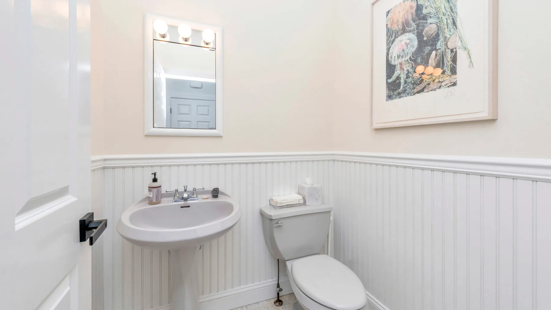 Un baño con lavabo de pared, inodoro y una lámina enmarcada.