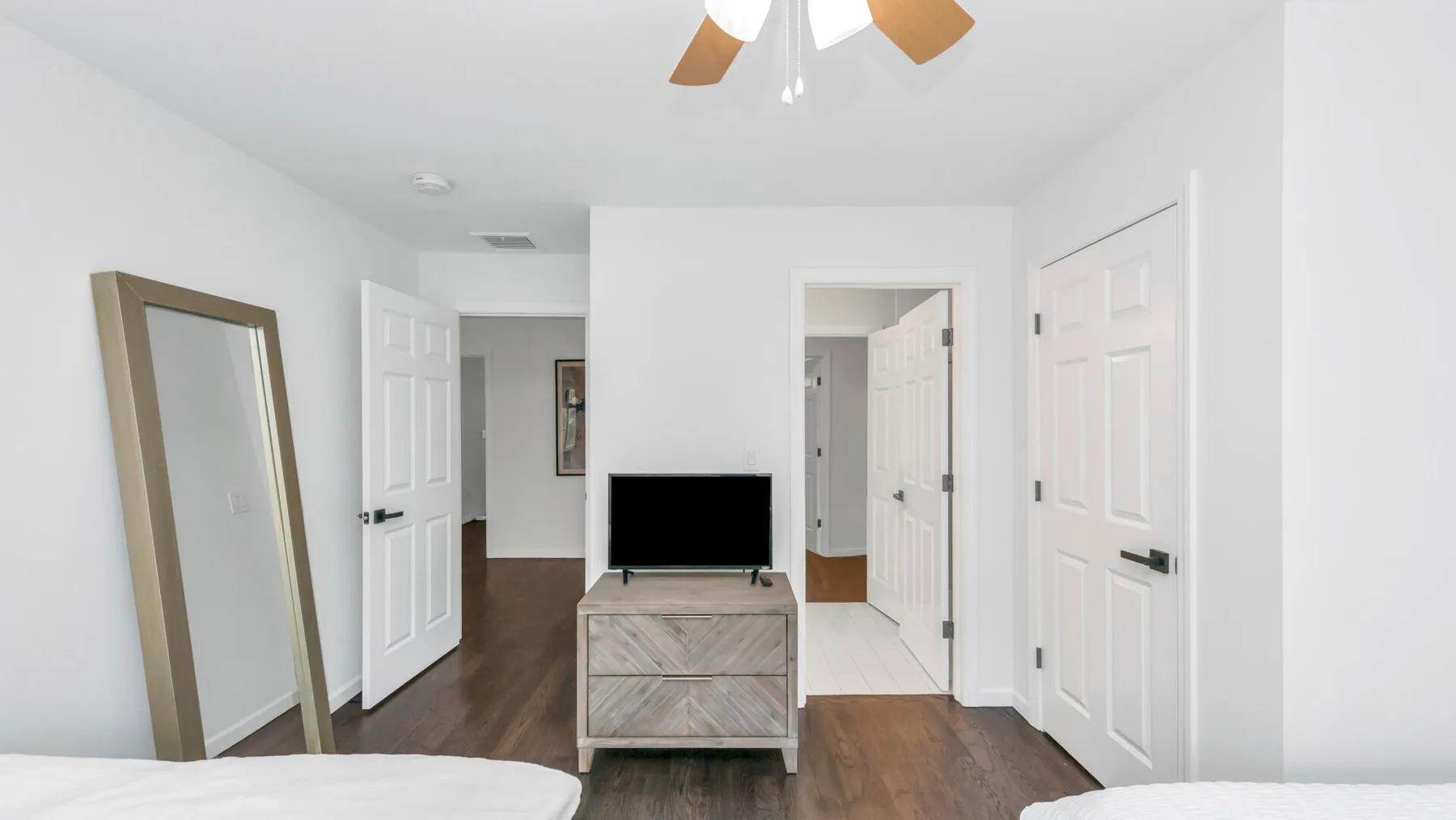 Un dormitorio luminoso con un televisor sobre una cómoda y varias puertas.