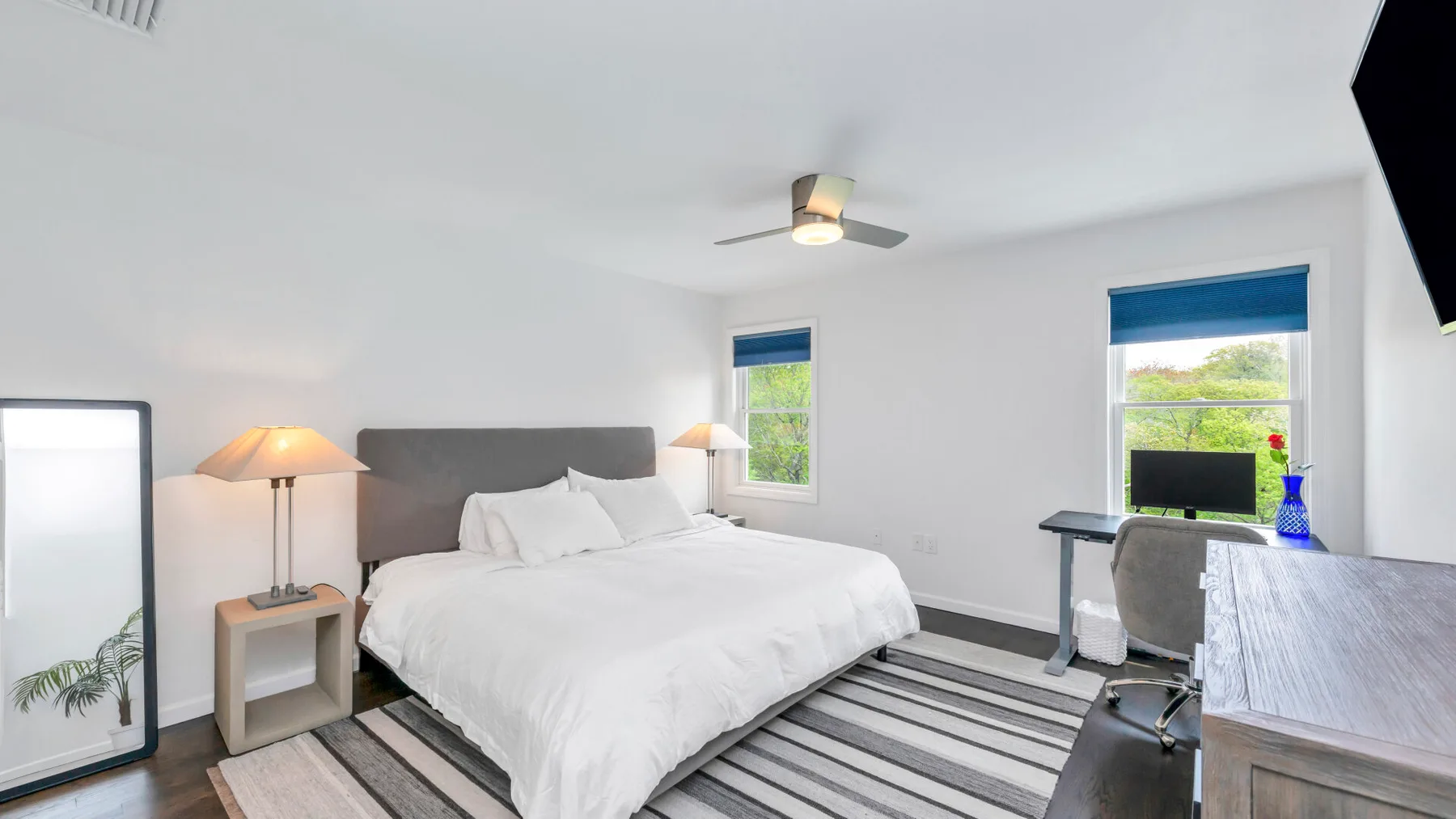 Un dormitorio luminoso con una cama tendida y un escritorio junto a la ventana.
